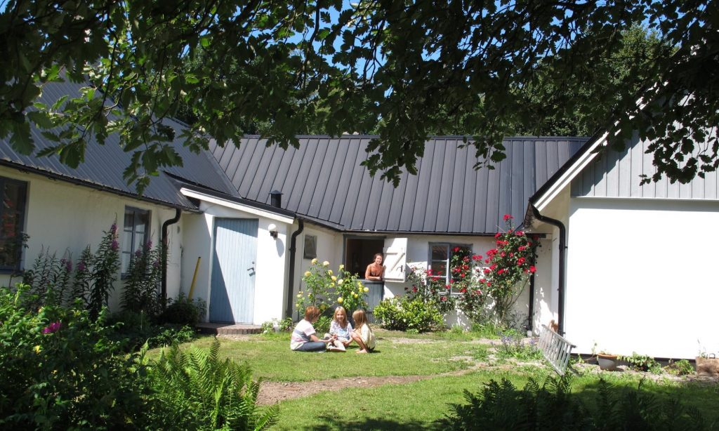 Det är en solig sommardag och barn sitter framför i-abbekas huset, en kvinna tittar ut genom dörren.